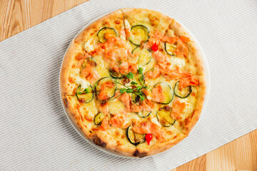 Pizza with zucchini, red fish and cheese, on a white plate, top view