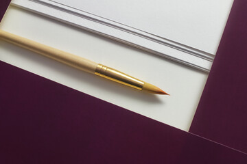 Close-up of a brush for painting near a folder with white paper on the table.
