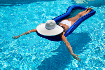 Beautiful woman in a white hat lies on a mattress in the pool and relaxes