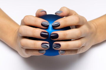 Gray-black manicure with silver stripes and drops on short square nails, close-up on a white background. Gray-blue color nails with a ball in his hands.