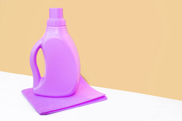 Purple bottle is standing on a purple bright rag for cleaning against a orange wall. Cleaning concept