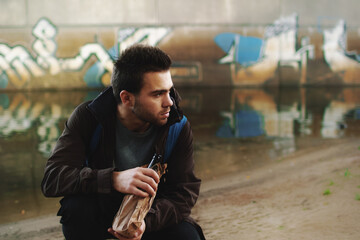 Close-up of a young brunette male alcoholic on the street under the bridge.