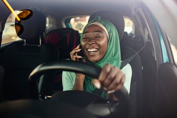 Beautiful muslim woman with toothy smile driving car and talking with smartphone. Young African Muslim woman driving a car. Muslim businesswoman on a business trip, driving a car