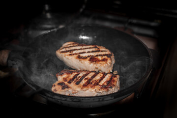 Juicy appetizing pork steaks on the grill in a cast-iron pan, home cooking.