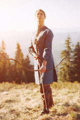 Woman shooting with a bow in the mountains. Young Caucasian female archer shooting with a bow at...