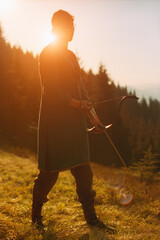 Woman shooting with a bow in the mountains. Young Caucasian female archer shooting with a bow at...