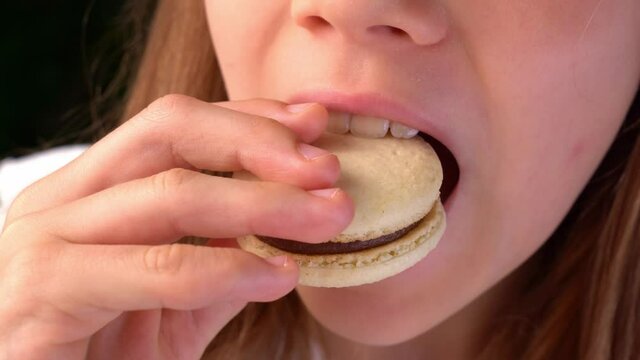 teen girl takes macaron from box and bites him.