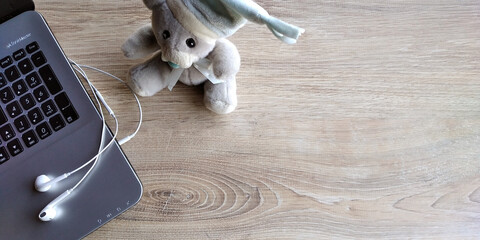 scrivania in legno chiaro con portatile, cuffie bianche e piccolo peluches. Spazio per scrivere.