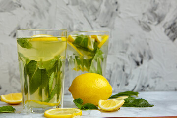 Fototapeta premium Refreshing drinks for summer, cold sweet and sour lemonade juice in the glasses with sliced fresh lemons. Refreshing summer drink. Traditional lemonade with lemon, mint and ice. Selective focus