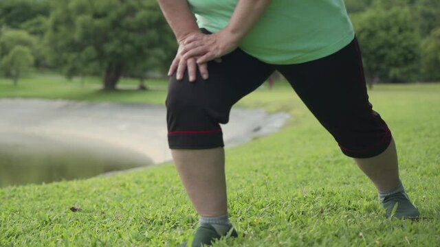 over weight female stretching her legs hand to Knee, standing legs stretch, cool down after morning exercise at the outdoor park, old age healthy life, lower body section, standing lunge practicing