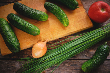 Cucumbers on a chopping Board, green onions and tomatoes on an old wooden table.