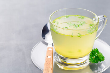 Chicken broth in a glass cup with chopped parsley, horizontal, copy space