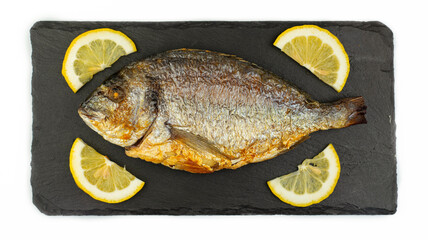 Baked cooked dorado fish and lemon lie on a black stone slate board