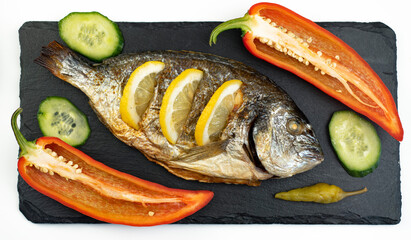 Baked cooked dorado fish and lemon lie on a black stone slate board