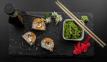 Sushi with eel and wakame hayashi salad lie on a black board made of stone. Top view