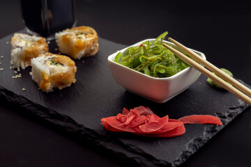 Sushi with eel and hayash wakamei salad lie on a black board made of stone slate