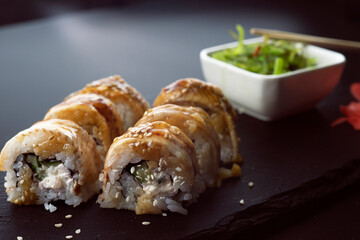 Sushi with eel and hayash wakamei salad lie on a black board made of stone slate