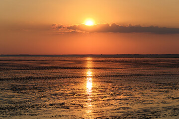Obraz premium Kleine Wolken vor der untergehenden Sonne über dem Wattenmeer vor der Nordseeinsel Spiekeroog - Stockfoto