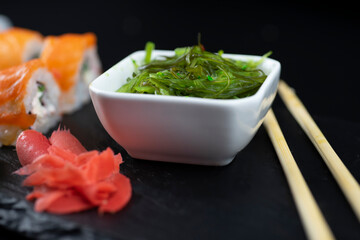 Sushi roll with salmon and wakame salad lie on a black board made of slate stone