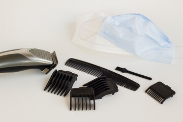 Slim Hair Clipper with stainless steel blades and different size combs of clipper and writing numbers on them on grey background with medical face mask.