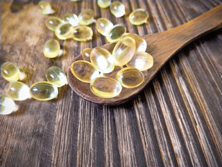 Vitamin D yellow pills on wood spoon on wooden background & soft sun light. Medicine gel tablets of vitamin d on table. Yellow vitamin D oil capsule keeps healthy while lack of sun - medicine concept