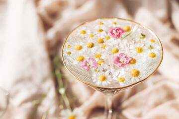Wildflowers in water in stylish wine glass on background of soft beige fabric. Tender floral aesthetic. Creative summer image with space for text. Bohemian mood
