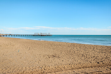 Beach and sea landscape in clear sunny day. Long wooden pier in the sea.