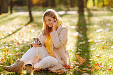 Smiling girl collects yellow leaves in autumn. Young woman enjoying autumn weather. Rest, relaxation, lifestyle concept.