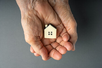 Inheritance concept. Elderly woman hands holds a little toy house. Inherited property idea. - obrazy, fototapety, plakaty