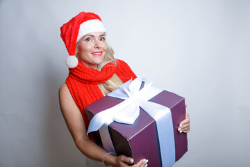 Blonde with long hair in a Santa hat, Big gift with a white bow in her hands. Studio, light background, Happy New Year greetings.