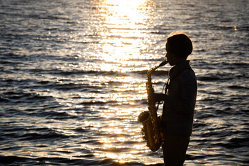 silhouette of a young musician at sunset, portrait of a boy playing the saxophone, romantic evening