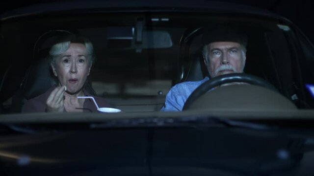 A Mature Caucasian Couple Sitting In Their Car Watching A Funny Movie At A Drive-in Theater.
