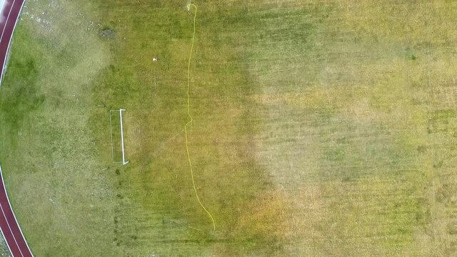 Top down aerial view of football field surface covered with green grass and sprinklers spraying water.