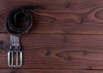 Old leather belt with buckle on an old wooden Board with space for text. Men's brown belt made of genuine leather with a metal buckle on a dark background. Genuine leather, handmade. Metal rivet.