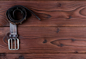 Old leather belt with buckle on an old wooden Board with space for text. Men's brown belt made of genuine leather with a metal buckle on a dark background. Genuine leather, handmade. Metal rivet.