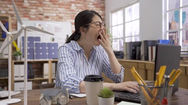 tired businesswoman snoozing and yawning at workplace. Bored sleepy asian chinese female architect sitting half asleep at desk. lazy woman engineer disinterested in boring routine on laptop computer