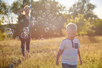 Fototapeta na wymiar Mom and baby blow soap bubbles on a sunny meadow in summer.