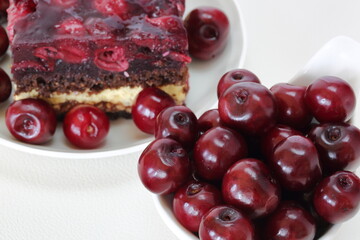 Fresh juicy cherries  in a bowl and cake with cherries on white plate close up