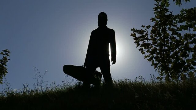 A sniper, wearing a camouflage suit, holding a weapon, rifle, sub-machine gun, tommy-gun, machine carbine in his hand, standing in the woods, througհ the forest - Slow Motion, Back Light, Silhouette
