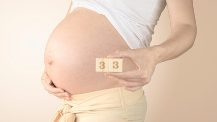 Pregnant young woman with pregnancy week number next to her belly. Photos of belly growth at 33...