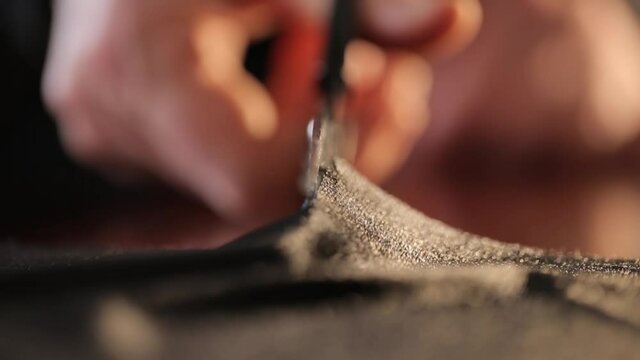 Female hands are cutting black fabric, scissors closeup. Women's clothing designer makes garment details from fabric in an atelier workshop. Part1