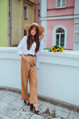 Young happy beautiful girl is walking in a shirt and pants with a bouquet of flowers of sunflowers on a city street