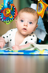 Cute caucasian baby boy lying down on colorful play mat with toys, during his tummy time.