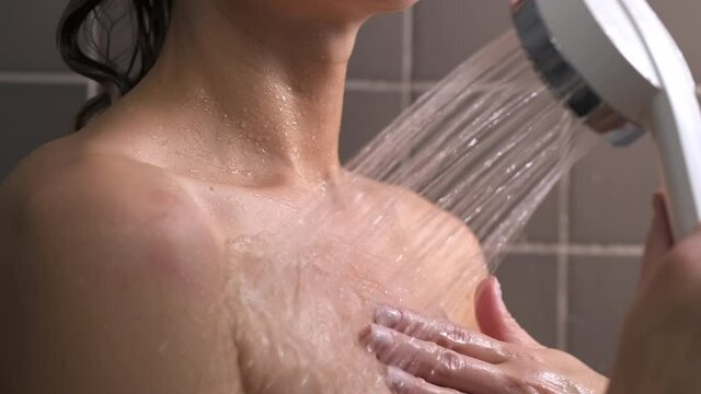 Attractive brunette middle-aged woman takes a shower. Woman washes her hair. Naked body. Grey tile on the walls. Taking care of skin, routine home treatments. Woman walks her hand over the wall.