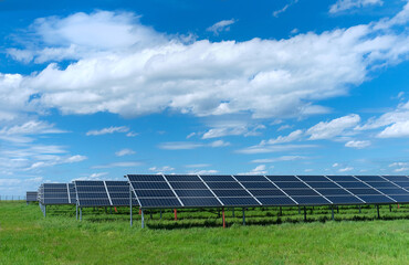 Solar power plant, blue solar panels on grass field under blue sky with clouds