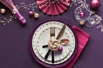 Christmas table setup with golden rim plates, golden utensils and dark red deco. Flat lay on purple linen textile.