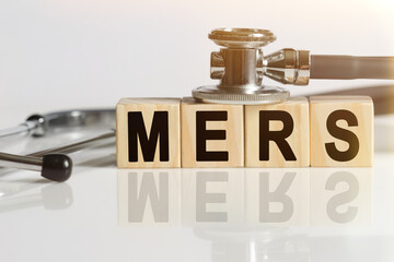 MERS the word on wooden cubes, cubes stand on a reflective white surface, on cubes - a stethoscope.