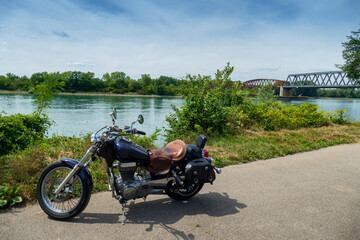 Fototapeta na wymiar Motorrad steht einsam am Rhein, Im Hintergrund die alte Brücke Wintersdorf