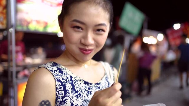 Cheerful Asian woman eating potato balls on street