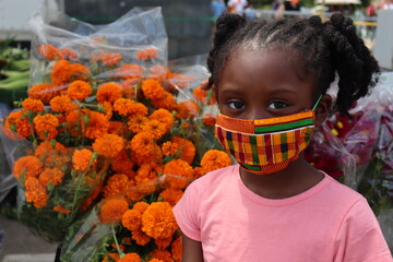 Close up of girl wearing colorful African fabric face mask with orange flower bouquet background
